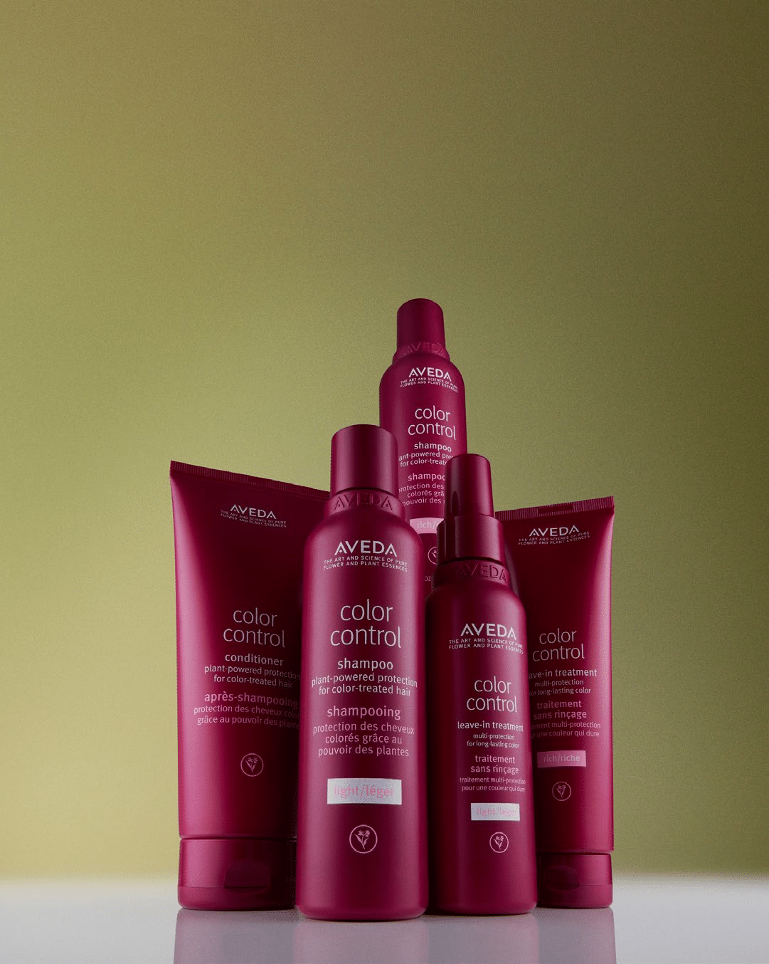 Fünf rosa Aveda Color Control Haarpflegeflaschen, darunter Shampoo, Spülung und Kuren, sind vor einem grün abgestuften Hintergrund angeordnet. Die Flaschen variieren in der Größe und sind mit weißer Schrift beschriftet.